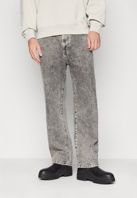 Jeans de mezclilla gris deslavado con corte recto y costuras en contraste. Combinados con zapatos negros de suela gruesa. Sudadera sencilla visible por encima.