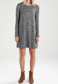 Abito lavorato a maglia con maniche lunghe in un motivo grisaglia, caratterizzato da una vestibilità ampia e che arriva a metà coscia. Abbinato a stivaletti marroni.