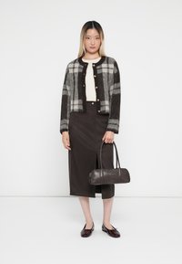 Brązowy sweter w kratę z guzikami, kremowy top, ciemnobrązowa spódnica z bocznym rozporkiem, czarna torba oraz bordowe buty z kokardkami.
