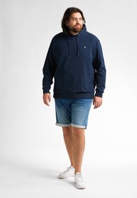 Hanorac bleu marin cu șnur, asortat cu pantaloni scurți din denim de un albastru deschis, răsuciți la margine. Adidași albi completează ținuta.