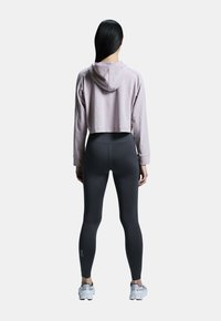 Světle fialová zkrácená mikina s kapucí, spárovaná s tmavě šedými legínami. Legíny mají bílé logo značky na spodní části nohy.