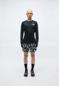 Schwarzes Langarmshirt, gemusterte Blumen-Shorts, schwarze Socken und schwarze Schuhe mit Akzenten. Glatter Stoff, sportliche Passform.