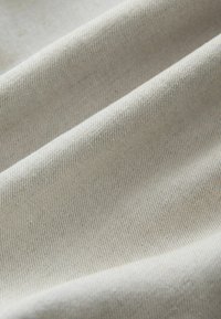 Tissu beige clair avec des motifs fins en sergé diagonal créant des plis et des ombres douces.