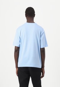 T-shirt en coton bleu clair avec une coupe décontractée, col rond et manches courtes, vu de dos. Design simple, sans motifs ni accents visibles.