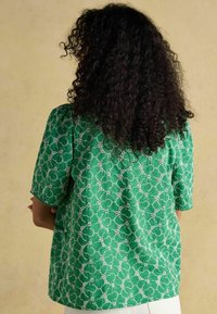 Blusa verde con maniche corte, caratterizzata da un motivo in pizzo floreale. Tessuto morbido, vestibilità comoda, scollo rotondo e dettagli testurizzati.