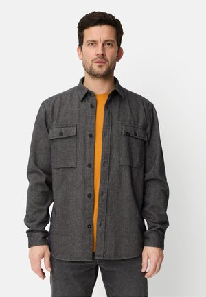 Grå flannelskjorte med to brystlommer og sorte knapper, båret over en sennepsgul skjorte. Lange ærmer og en afslappet pasform.