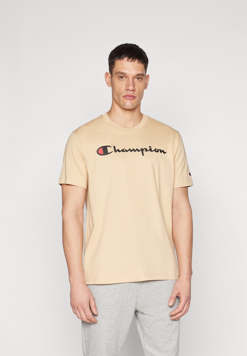Beige Baumwoll-T-Shirt mit Rundhalsausschnitt und kurzen Ärmeln. Mit einem schwarzen "Champion"-Logo auf der Vorderseite, mit einem roten Akzent im "C."