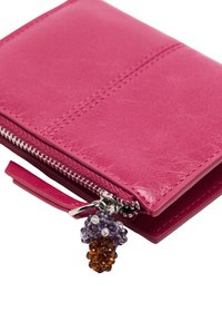 Fuksjowy skórzany portfel z zamkiem błyskawicznym, ozdobiony koralikowym brelokiem w odcieniach fioletu i pomarańczu. Gładka tekstura i minimalistyczny design.