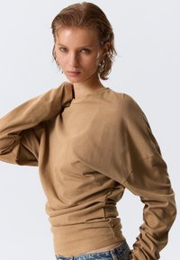 Καφέ μακρυμάνικο πουκάμισο κατασκευασμένο από απαλό ύφασμα, με άνετη εφαρμογή και ριμπ τελείωμα. Λείο υφή με ραφές ώμων που πέφτουν χαμηλά.