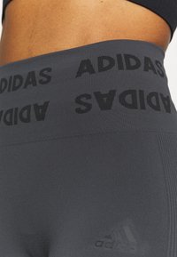 Ciemnoszare legginsy sportowe z szerokim paskiem w talii, z czarnym logo "ADIDAS", gładką teksturą i subtelnym tonalnym logo na biodrze.