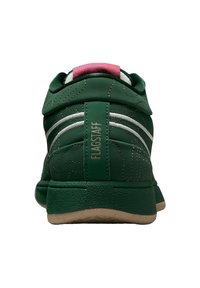 Grüner Sportschuh mit weißen Streifen, strukturierter Oberfläche und pinkfarbenem Akzent an der Ferse. Verfügt über goldene Schriftzüge und Konturlinien am Obermaterial.