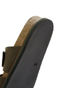 Sottopiede in sughero marrone, accento verde e suola in gomma nera texturizzata, con un design a fascia larga. Il materiale sembra morbido e flessibile.