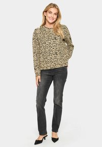 Felpa con scollo rotondo in stampa leopardata beige e nera, abbinata a jeans scuri e tacchi a punta neri. Texture liscia, vestibilità rilassata.
