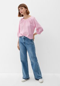 Lichtroze, getextureerde blouse met een ronde hals en pofmouwen, gecombineerd met hoge, wijde spijkerbroeken in blauw en witte sneakers.