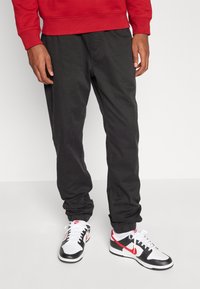 Svarta bomullsshorts med elastisk midja, tillsammans med svart-vita sneakers med röda detaljer. Röd sweatshirt knuten i midjan.