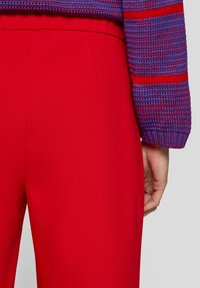 Red trousers with a smooth texture and elastic waistband, paired with a knitted purple and red striped sweater.