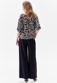 Zwarte en beige geblokte top met een losse pasvorm, brede mouwen, gecombineerd met zwarte, vloeiende wijde broeken. Minimalistisch ontwerp en soepele textuur.