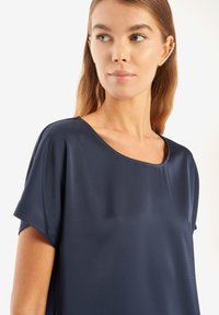 Marinfärgad kortärmad blus med rund halsringning, slät textur och avslappnad passform. Anmärkningsvärda detaljer inkluderar subtil lyster och mjukt fall.