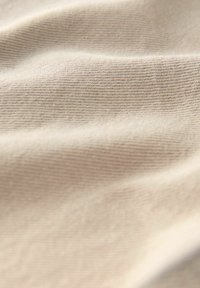 Tissu beige avec une surface lisse et légèrement texturée, présentant des stries horizontales subtiles et des plis doux.