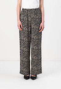 Pantalons évasés en imprimé zèbre noir et crème, dotés d'une taille élastique et d'un tissu lisse et léger. Assortis avec des chaussures noires.