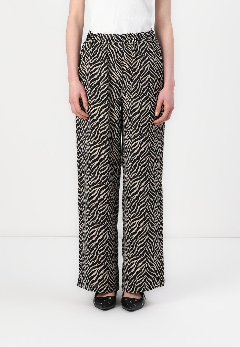 Pantalons évasés en imprimé zèbre noir et crème, dotés d'une taille élastique et d'un tissu lisse et léger. Assortis avec des chaussures noires.