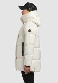 Biela nadýchaná bunda s vysokým golierom, kapucňou a bočnými vreckami na zips. Na ľavom rukáve je čierna nášivka s logom. Hladká, lesklá textura.