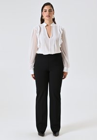 Blusa bianca con dettagli a ruches e scollo a V, abbinata a pantaloni neri su misura e scarpe nere a punta. Tessuto morbido e design strutturato.