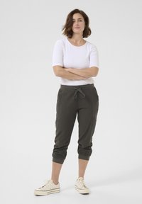 Ciemnozielone spodnie do kostek z elastycznymi mankietami i sznurkiem w talii, zestawione z dopasowaną białą bluzką z krótkim rękawem i jasnymi sneakersami.