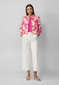 Różowa kurtka w kwiatowy wzór z okrągłym kołnierzem, noszona na jednolitym różowym topie. Połączona z białymi szerokimi spodniami i sandałami na obcasie.