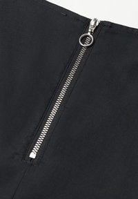 Tissu noir avec une fermeture éclair centrale argentée à l'arrière, dotée d'une languette métallique et de dents fonctionnelles, sur une surface lisse.