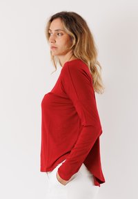 Maglietta rossa a maniche lunghe realizzata in tessuto morbido e leggero. Presenta una vestibilità rilassata, orlo arrotondato e una leggera caduta alle maniche.