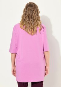 Lockere, kurzärmelige Bluse aus leuchtend pinkem Baumwollstoff. Der Saum reicht bis zur Mitte des Oberschenkels, hat eine glatte Textur und keine sichtbaren Muster oder Akzente.