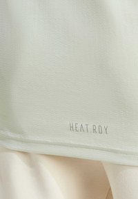 Světle zelený sportovní top s texturovaným vzorem, se znakem "HEAT.RDY" na spodním okraji. Měkká, prodyšná tkanina pro maximální výkon.