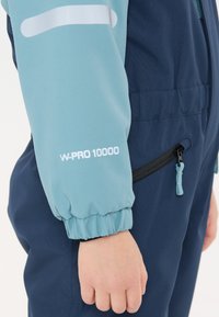 Blå skidjacka med ett mjukt skalmaterial och en åtdragen mudd. Ärmen visar "W-PRO 10000" i vitt, med en sidoficka med blixtlås.