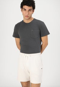 T-shirt grigia in cotone con maniche corte e taschino sul petto abbinata a pantaloni corti beige chiaro con fascia elastica in vita e cordoncino.