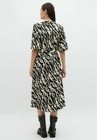 Černé a krémové vzorované šaty s krátkými rukávy, páskem v pase a splývavým střihem, doplněné černými kozačkami do kolen.