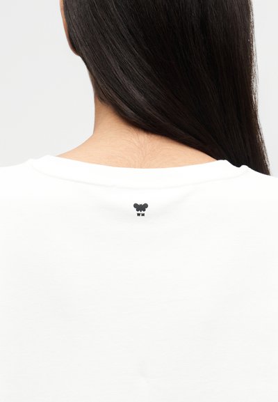 Λευκό βαμβακερό t-shirt με στρογγυλή λαιμόκοψη, με μικρό μαύρο λογότυπο πεταλούδας και τα γράμματα «WM» από κάτω στην πλάτη. Ομαλή υφή.