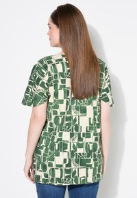 Camiseta de manga corta en tonos verde y crema con un diseño abstracto, elaborada en una tela suave y ligera. La parte trasera presenta un dobladillo redondeado.