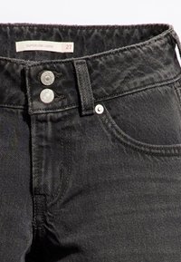 Jean en denim noir à la taille avec fermeture à bouton, passants de ceinture, poche avant et étiquette portant la mention "SUPERLOW LOOSE 27."