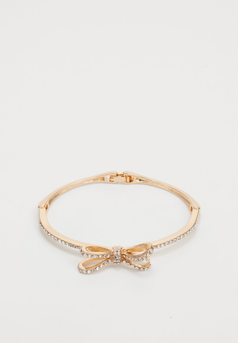 Bracciale rigido in tono oro con un design a fiocco decorato con strass trasparenti lungo la fascia per un tocco di brillantezza. Texture metallica liscia.