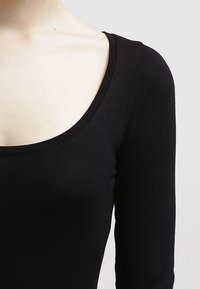Top negro ajustado de manga larga con escote redondeado, fabricado en una tela suave y elástica, ideal para llevar en capas o como prenda independiente.