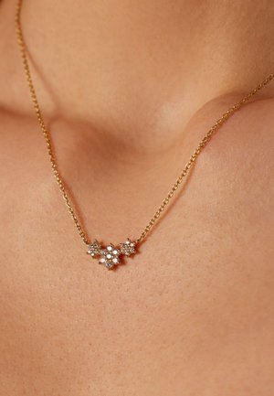 Gold chain necklace with three small flower-shaped pendants adorned with clear gemstones on a person's collarbone.