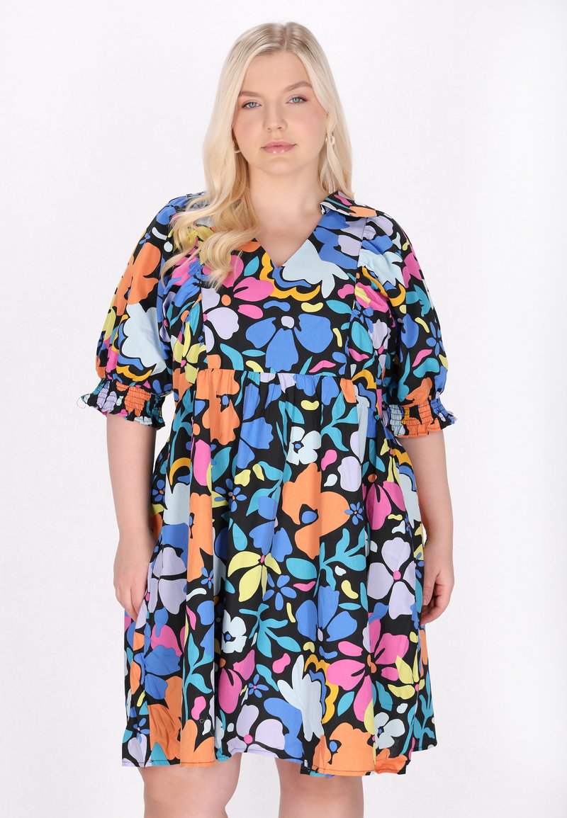 Rochie scurtă colorată cu un bază neagră, având modele florale mari în nuanțe vibrante de albastru, roz, portocaliu și galben. Mâneci bufante.