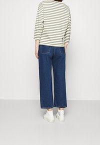 Stribet grøn og hvid langærmet skjorte parret med brede mørkeblå jeans og hvide sneakers, set fra ryggen.