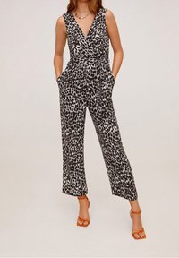 Combinaison à imprimé animal noir et blanc avec un décolleté en V profond, des jambes larges, des poches et une taille à nouer. Portée avec des sandales orange à lanières.