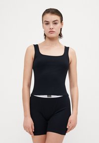 Juoda įsiūta tank top su kvadratiniu iškirpimu, derinama su juodais šortais su baltu juosmens etikete. Lygus paviršius ir prigludęs dizainas.