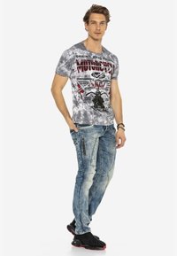 Graue Batik-T-Shirt mit Motorradgrafiken in Rot und Schwarz; kombiniert mit hellblauen Patchwork-Jeans und schwarzen Sneakers mit Nieten.