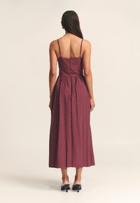 Długa bordowa sukienka w białe groszki, z cienkimi ramiączkami typu spaghetti i dopasowanym gorsetem przechodzącym w rozkloszowaną spódnicę.