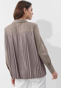 Langarmhemd mit einem zweifarbigen Design und glattem Vorderteil sowie plissiertem R�ücken. Die Farbe ist gedecktes Taupe mit knopfverzierten Manschetten.