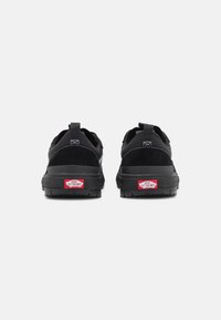Baskets noires présentant une combinaison de matériaux en daim et en mesh, une grande semelle en caoutchouc et un logo rouge "Vans Off The Wall" au talon.